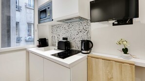 A modern kitchen with a built-in microwave, a flat-screen TV, and a coffee maker. - Cocooning studio - 2P - Center of Paris (Paris)