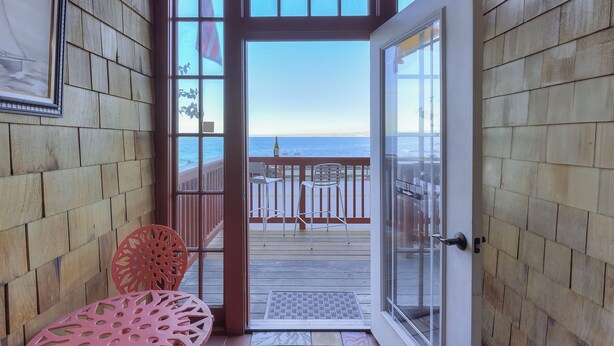 Un interior de madera con un ventanal de vidrio que da a un balcón con vistas al mar.