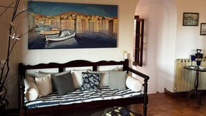 A cozy living room with a sofa, a painting of a harbor, and a small table with a kettle. - Eagle Nest Skiathos (Skiathos)