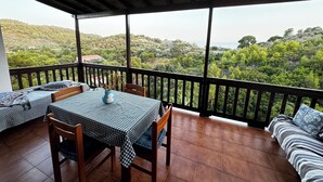 A balcony with a checkered table and chairs, a sofa, and a view of a hilly landscape. - Eagle Nest Skiathos (Skiathos)