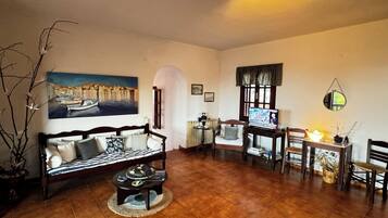 Uma sala de estar acolhedora com sofá, mesa de centro, televisão e um canto de jantar com cadeiras e mesa.