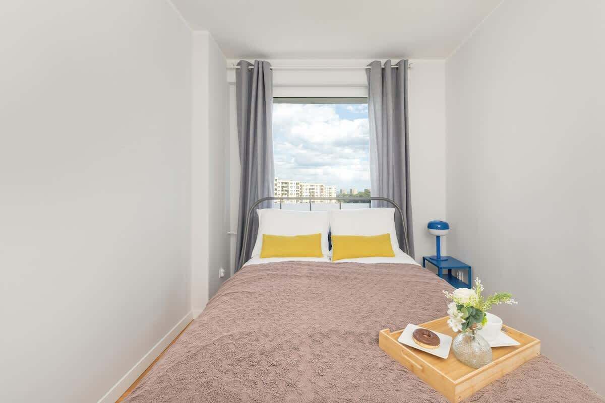 Une chambre à coucher avec un lit, une table de chevet, un plateau avec un gâteau et des fleurs, et une fenêtre avec des rideaux.