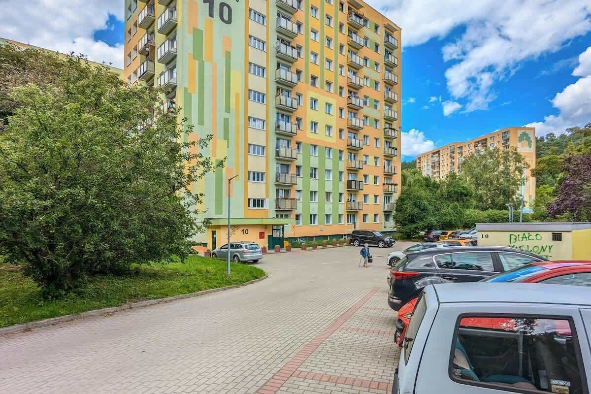 Un immeuble résidentiel à plusieurs étages, doté de balcons, d’une allée pavée et de voitures garées.