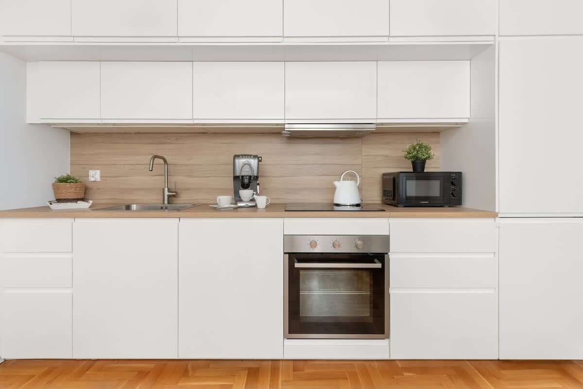 A modern kitchen with white cabinets, a stainless steel oven, a coffee maker, a kettle, and a microwave.