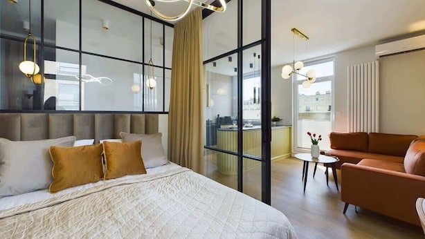 Una habitación de hotel moderna con una cama grande, un sofá, un balcón con vistas y una zona de comedor.