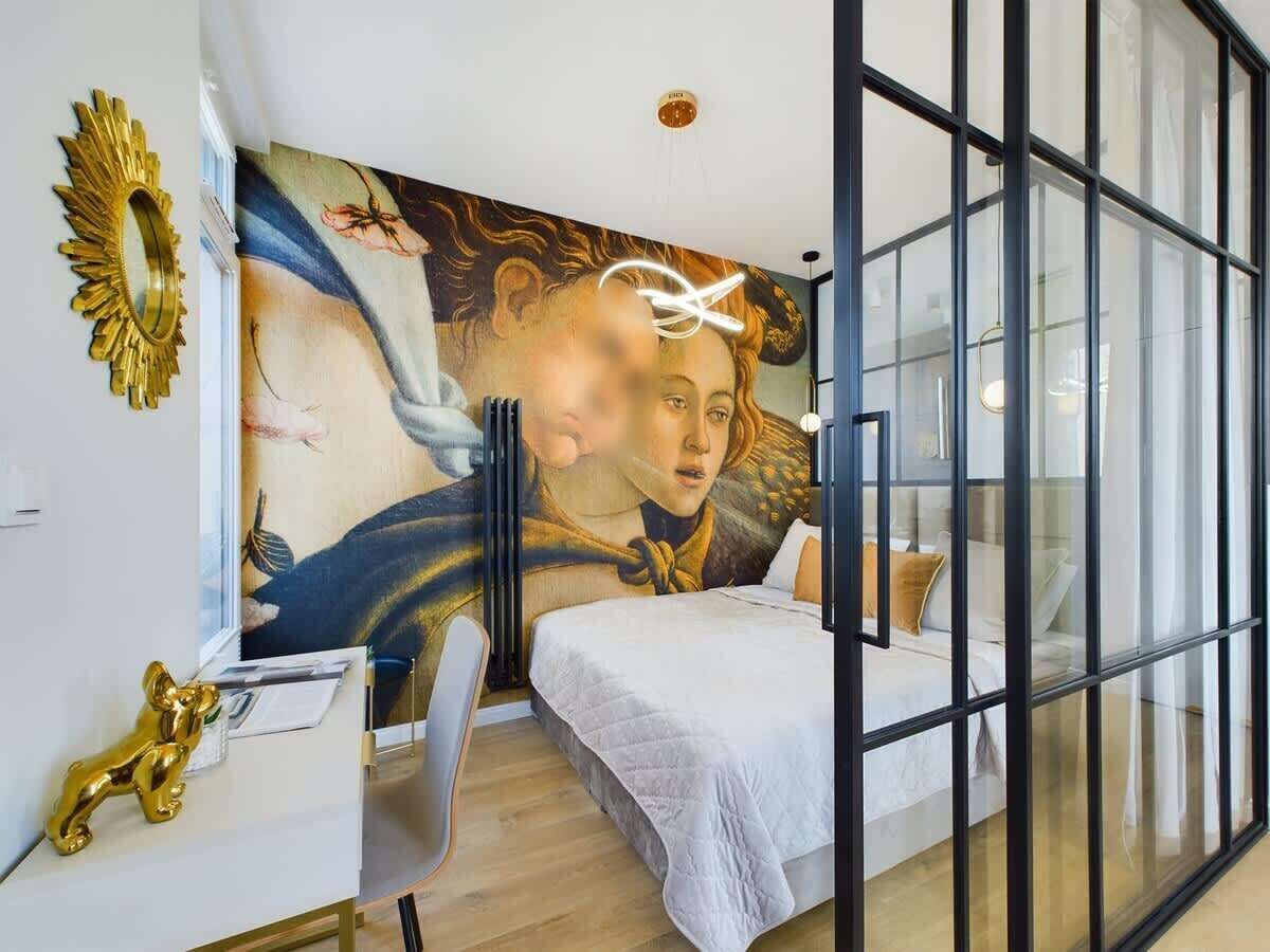A modern bedroom with a large mural, a desk, and a bed with a view through glass walls.