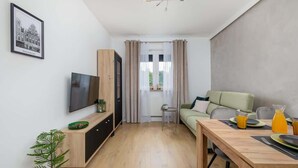 Una sala moderna con televisor, sofá, mesa de comedor y un ventanal con cortinas.