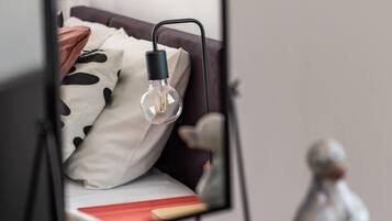 Een bed met een metalen frame, een hangende gloeilamp en een klein beeldje op een houten oppervlak.