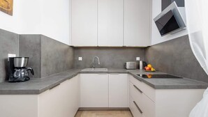 Una cocina moderna con cafetera integrada, un lavamanos y una pequeña encimera con frutas.