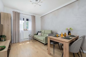 A modern living room with a wooden dining table, a green sofa, and a small side table.