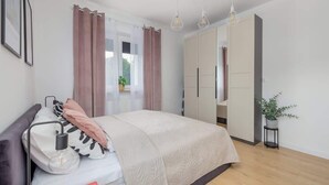 Un dormitorio con cama, lámpara de noche, cortinas, armario y una planta en maceta.