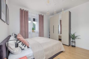 A bedroom with a bed, bedside lamp, curtains, wardrobe, and a potted plant.
