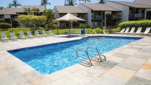 A swimming pool with a tiled edge, lounge chairs, and a person in a blue shirt.