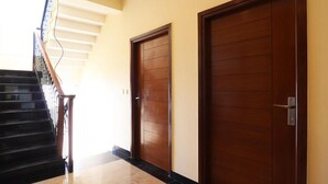 A hallway with two wooden doors, a staircase with black railings, and a light-colored floor. - Hotel Mussoorie Heights (Dehradun)