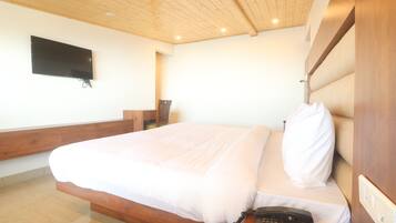 A bedroom with a bed, a telephone, a television mounted on the wall, and a wooden ceiling.