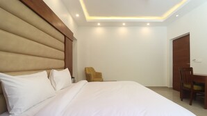 A bedroom with a large bed, a wooden headboard, a wooden desk with a chair, and a door. - Hotel Mussoorie Heights (Dehradun)