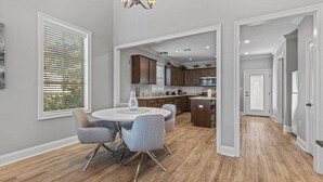 Uma cozinha moderna com armários de madeira, uma sala de jantar com mesa e cadeiras redondas, e um corredor que dá acesso a outros cômodos.