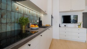Une cuisine moderne dotée d’une grande fenêtre, de meubles blancs, d’un plan de travail noir et d’un téléviseur à écran plat fixé au mur.