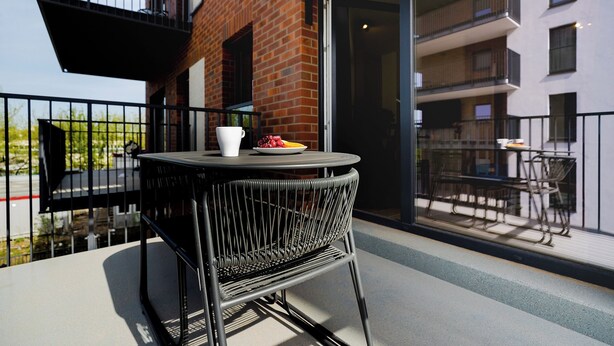 Un balcon avec une table ronde et des chaises, une tasse blanche et une assiette de fraises.