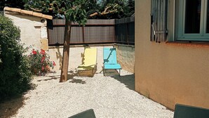 A patio area with a table and chairs, a small garden with red flowers, and a wooden fence in the background. - Charmant Studio AU Calme Avec Terrasse ET Parking (Fontvieille)