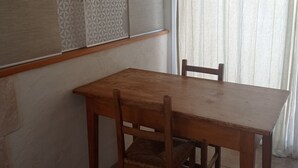 A wooden dining table with chairs in a room with a patterned wall and a window with sheer curtains. - Charmant Studio AU Calme Avec Terrasse ET Parking (Fontvieille)