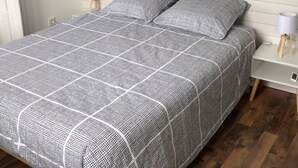 A bed with a checkered bedspread, two bedside tables with lamps, a wooden floor, and a wall with horizontal lines and a circular mirror.