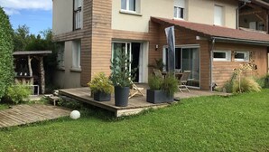 A two-story house with a wooden deck, potted plants, and outdoor furniture.