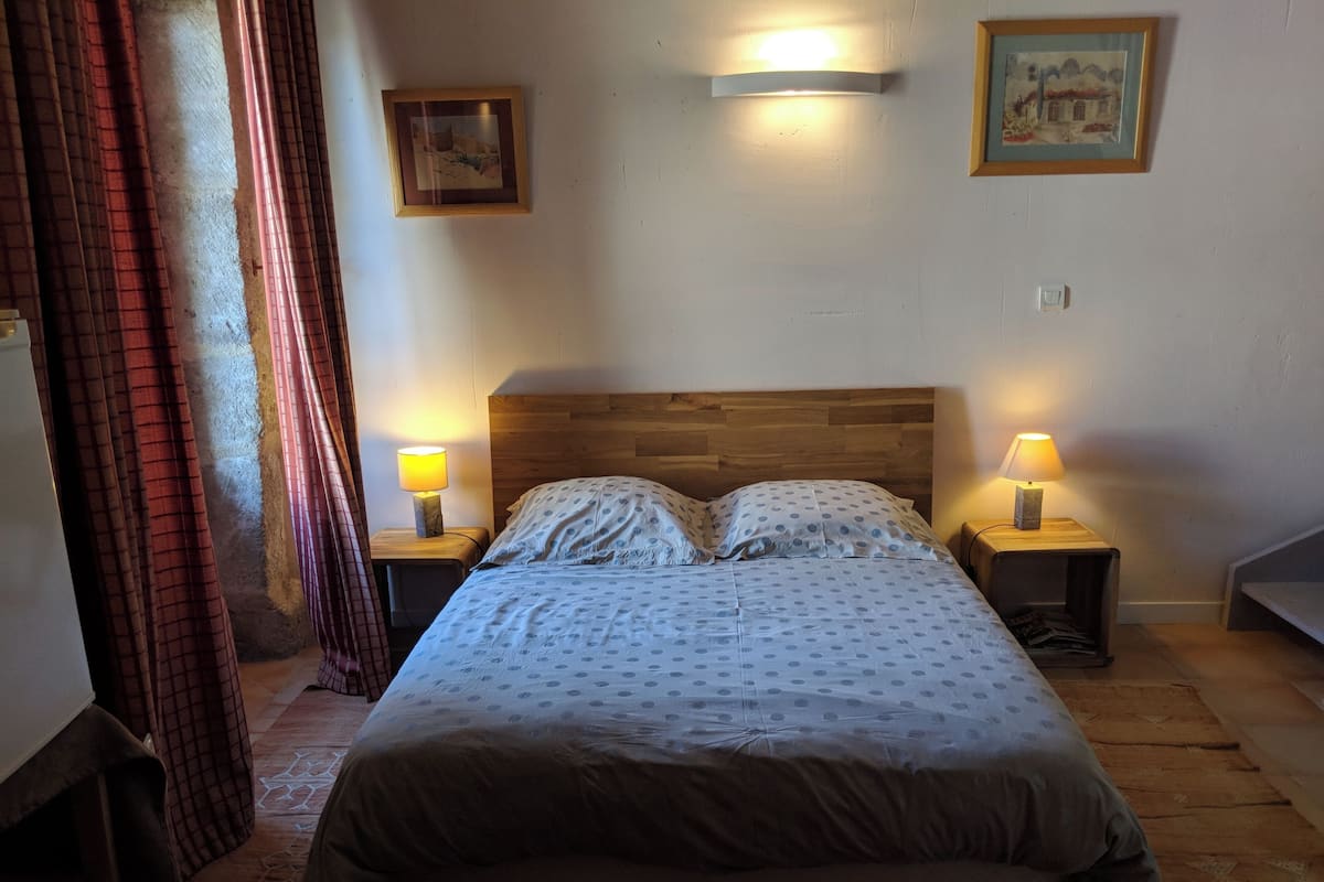 A bedroom with a wooden headboard, two bedside lamps, a bed with a patterned duvet, and a framed picture on the wall.
