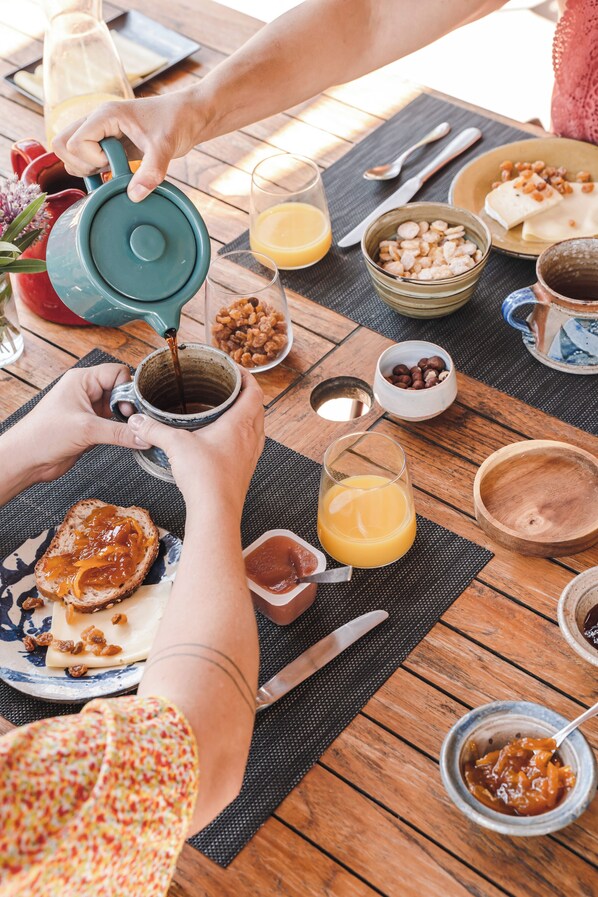 Une table de petit-déjeuner avec une table en bois, une théière, une tasse, un verre de jus d’orange et divers aliments.