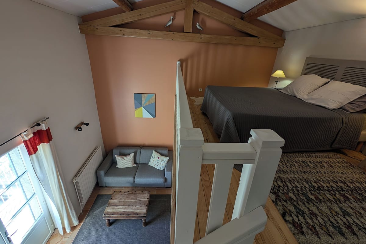 A bedroom with a bed, a sofa, a wooden ceiling, and a window with curtains.