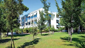 Un bâtiment moderne doté de nombreux balcons, entouré d’un espace verdoyant bien entretenu, agrémenté d’arbres.