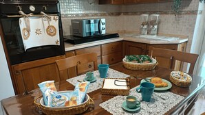 A kitchen with wooden cabinets, a stove, a microwave, and a dining table set with breakfast items. - Tra Pirandello e Leopardi B&B (Naples)