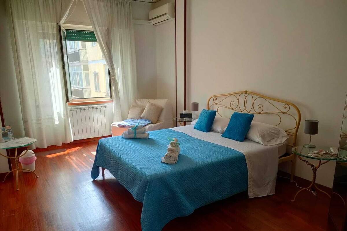 Un dormitorio ordenado con cama, mesitas de noche y una ventana con cortinas.