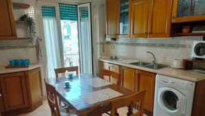 A kitchen with wooden cabinets, a washing machine, a sink, and a dining table with chairs. - Tra Pirandello e Leopardi B&B (Naples)