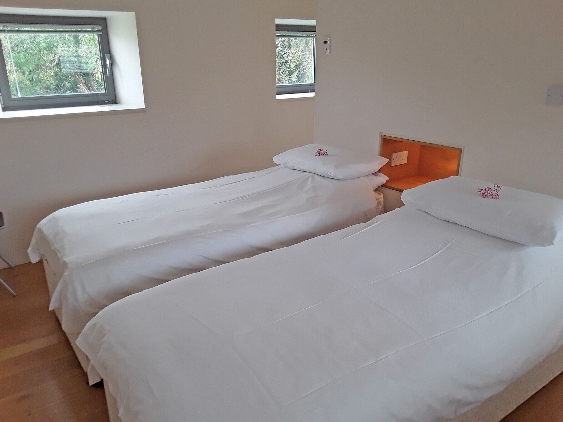 A bedroom with two single beds, each with white bedding and pillows, a wooden headboard, and a small window with a view of trees.