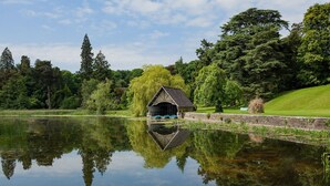Un paisaje tranquilo junto al lago con una pequeña estructura de madera, probablemente un cobertizo para botes, rodeado de exuberante vegetación y árboles.