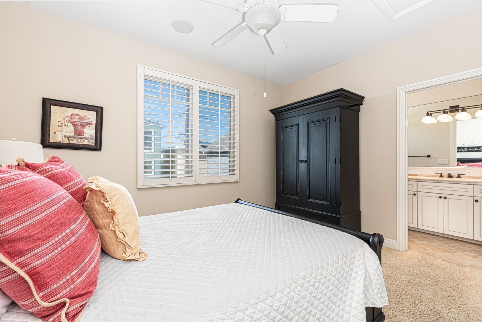 A bedroom with a bed, a wardrobe, a window with blinds, and a bathroom with a mirror and sink.