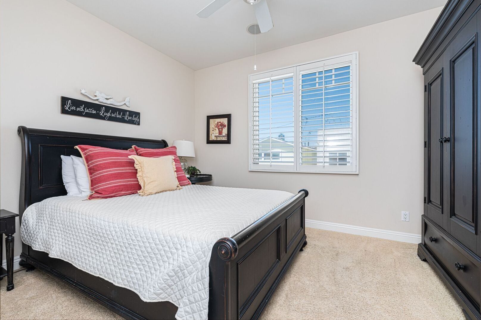 A bedroom with a bed, a nightstand, a dresser, a window with blinds, and a ceiling fan.