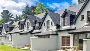 Una hilera de casas blancas de tejados oscuros y ventanas de madera, cada una con un pequeño patio y una mesa de picnic.
