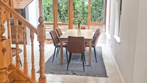 Un comedor con una escalera de madera, un ventanal con vistas a zonas verdes y una mesa con sillas.