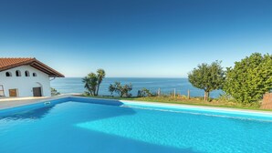 A pool with a clear view of the ocean, a white building with a red roof, and green trees. - Zeruhaundi - baskeyrentals (Biscay)