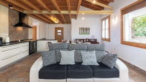 A modern kitchen with wooden beams, a dining area with a sofa, and a view of greenery through a window. - Zeruhaundi - baskeyrentals (Biscay)