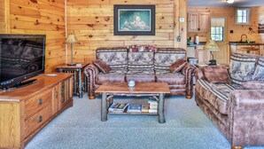 L’intérieur chaleureux d’un chalet, avec un décor en bois, un ensemble de canapés, un téléviseur et un tableau encadré au mur.