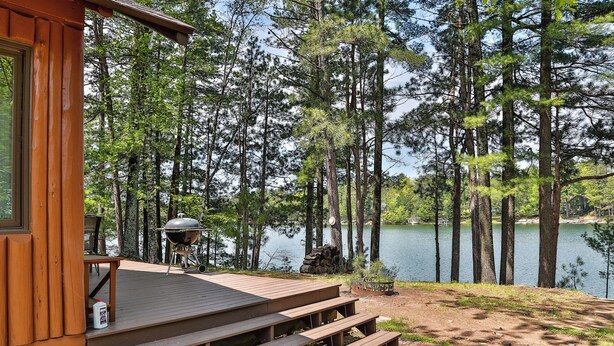 Une cabane dotée d’une terrasse donnant sur un lac, entourée de grands pins.