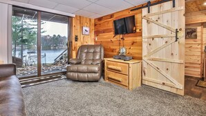 Ein gemütliches Blockhauss-Interieur mit einem Ledersessel, einem kleinen Holztisch mit Fernseher und einer großen Holztür.
