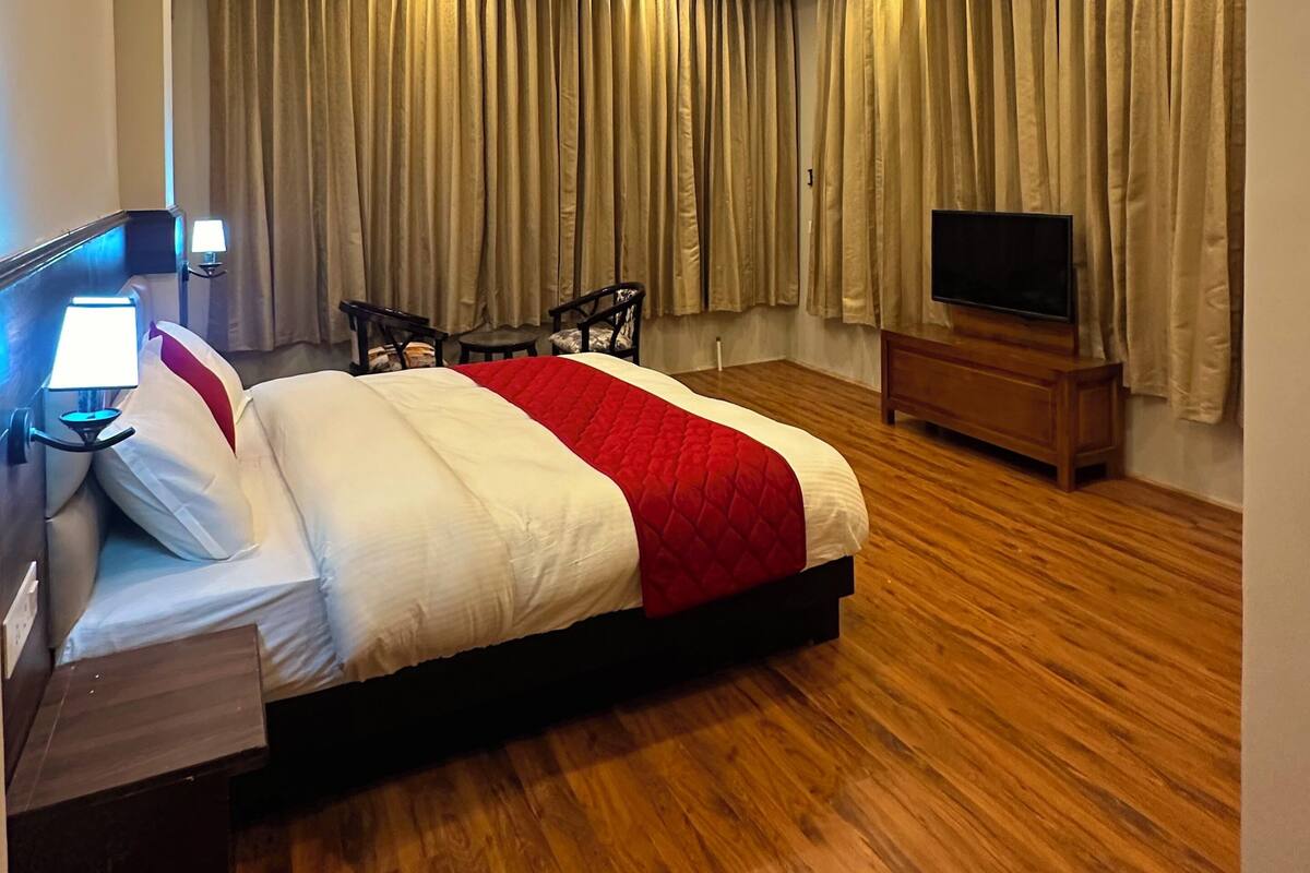 Ett modernt hotellrum med en stor säng, trägolv, en platt-TV och ett skrivbord med en lampa.