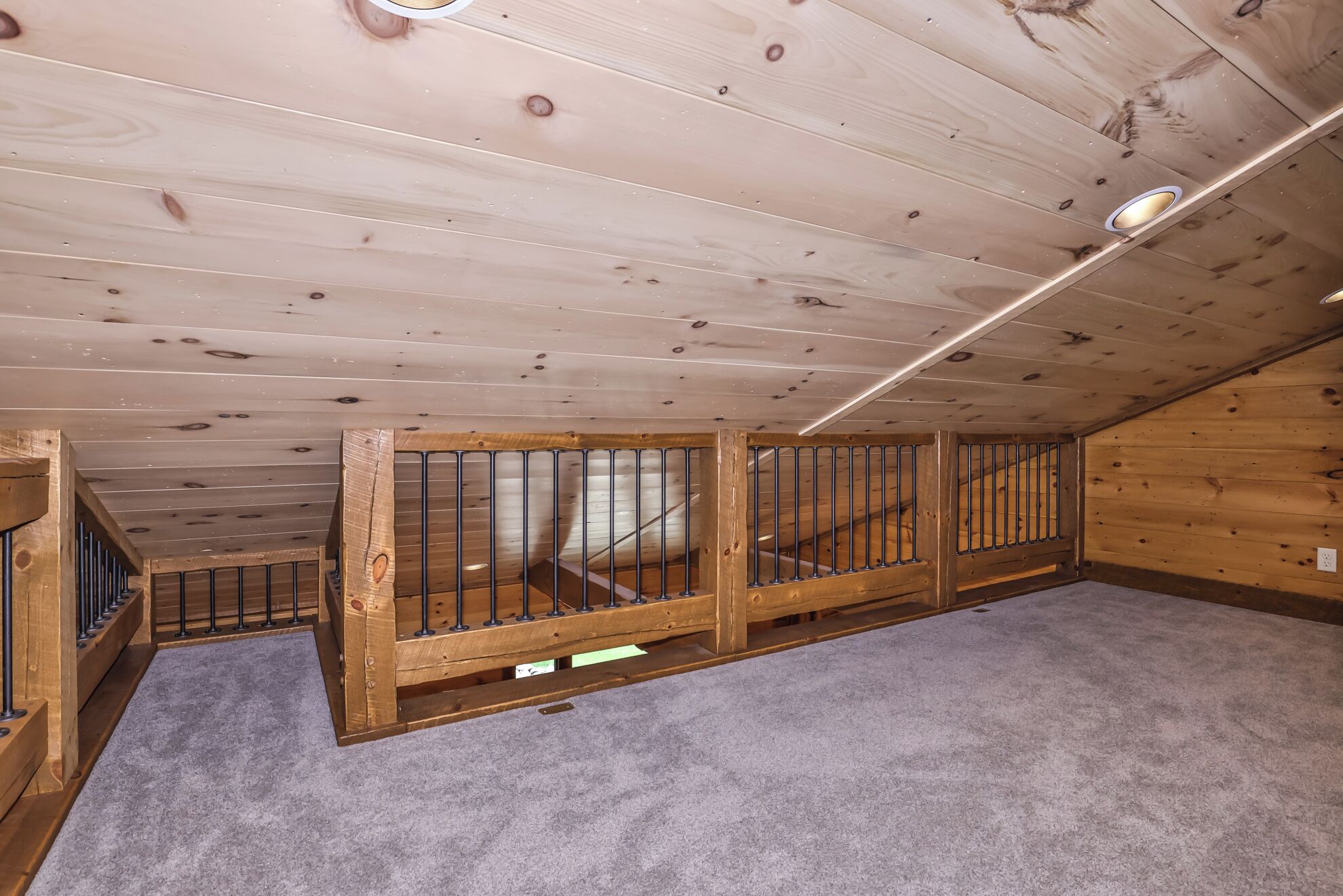 A wooden attic room with a sloped ceiling, a built-in wooden bench along one wall, and a carpeted floor.