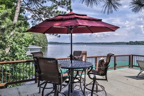 Una terraza con mesa y sillas, un paraguas rojo y vistas a un lago.
