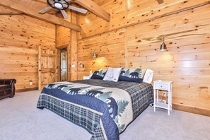 Un dormitorio de cabaña de madera con cama, mesitas de noche y ventilador de techo.