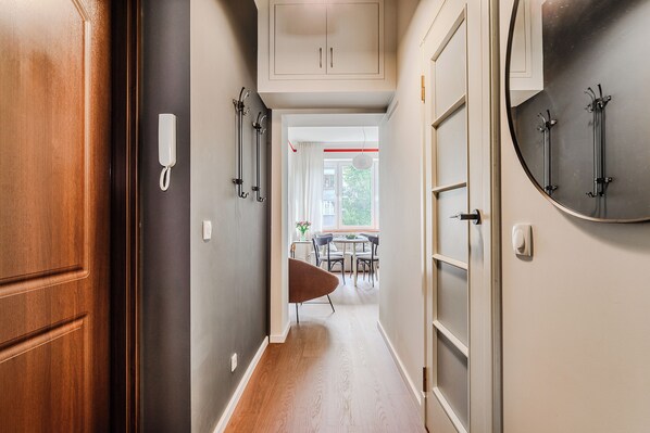 A hallway with a wooden door, a white wall with a phone, and a dining area with a table and chairs. - ShortStayPoland Francuska B161 (Warsaw)